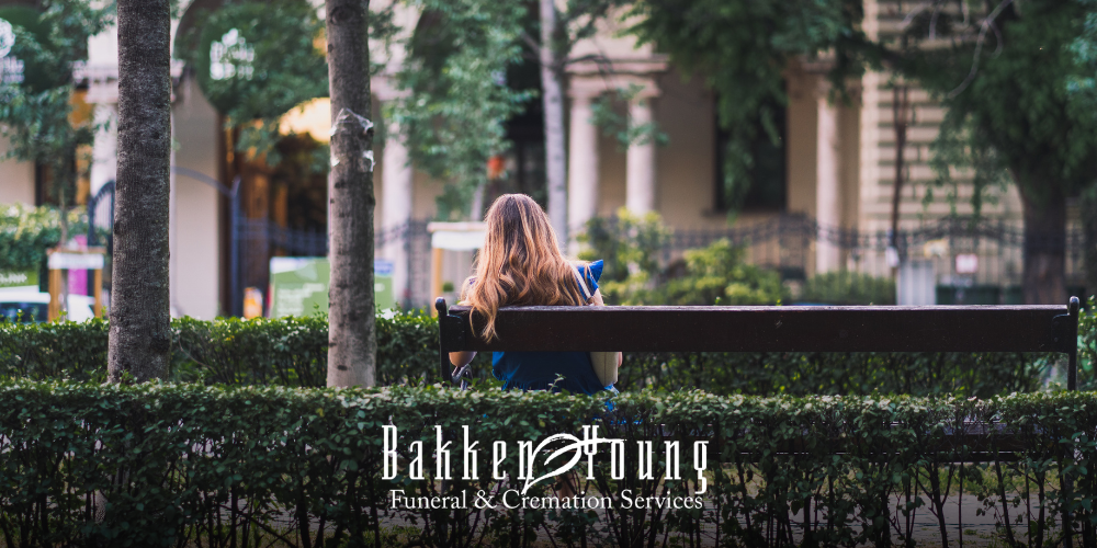 “Person sitting alone on a bench while others walk by, symbolizing still grieving when others move on”