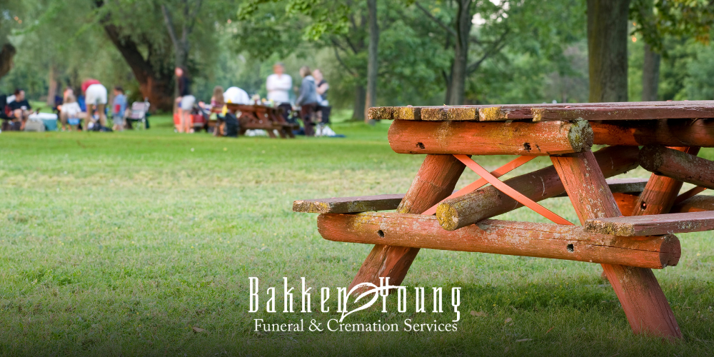 Picnic table at a park with simple food, drinks, and people gathered in a relaxed summer setting